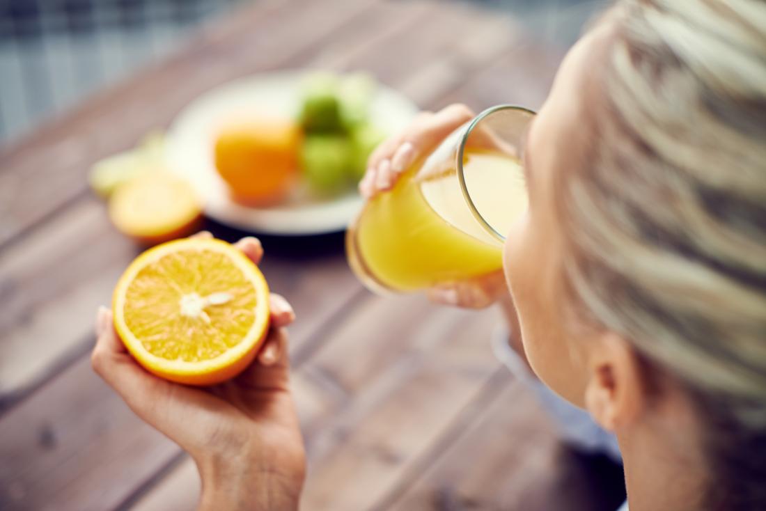 a woman drinking orange juice and holding an orange